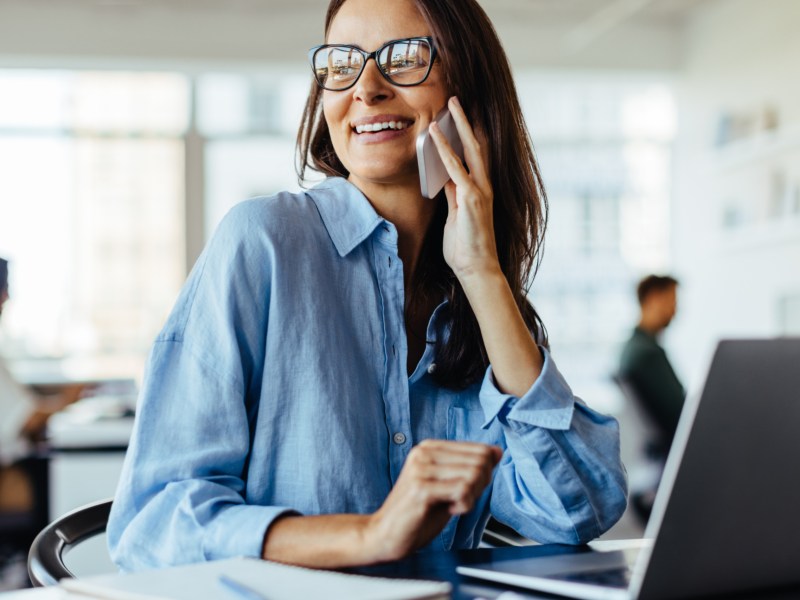 Frau am Arbeitsplatz hat ein Handy in der Hand und telefoniert.