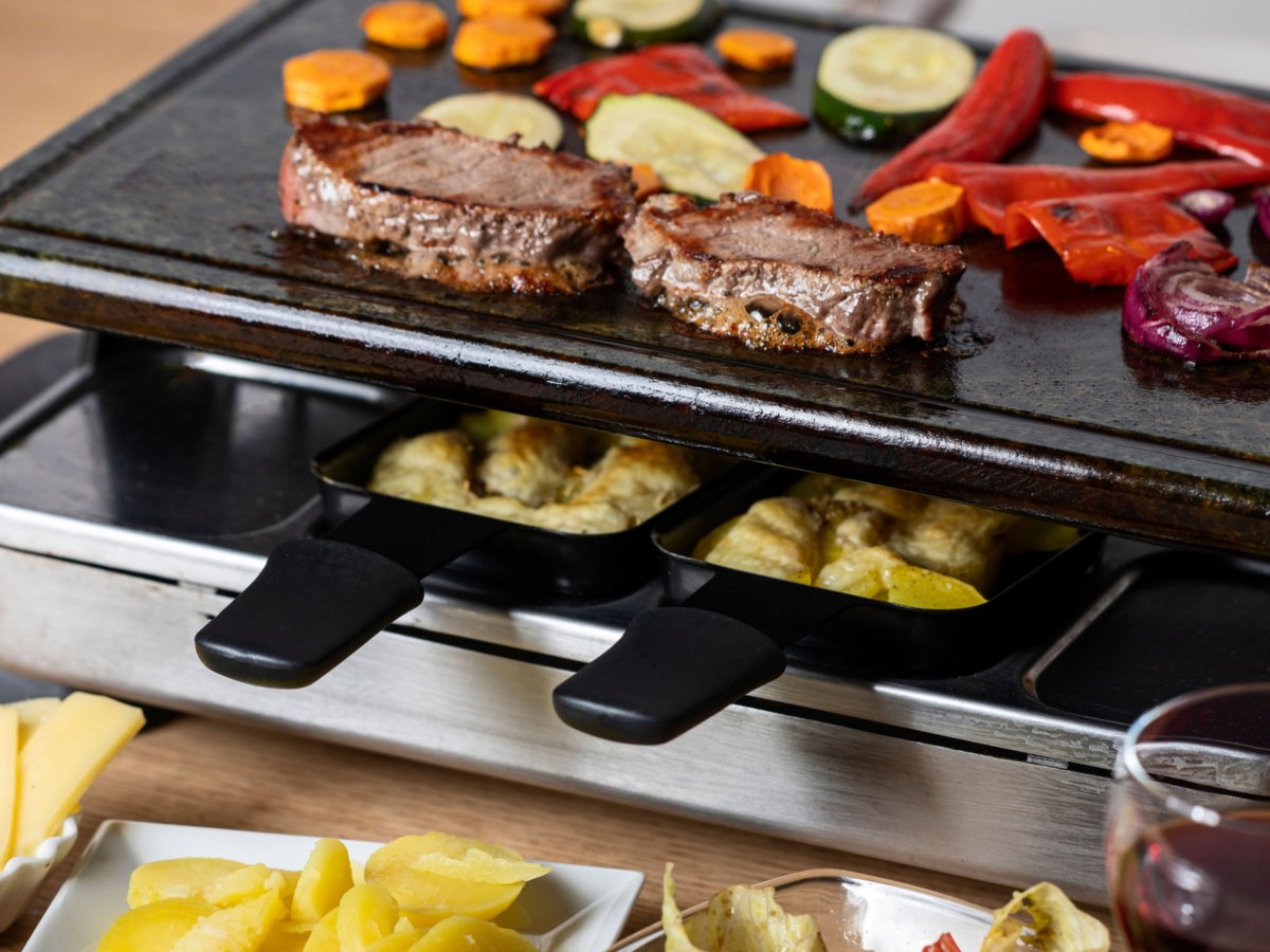 Raclette Mit 2 belegten Pf&auml;nnchen und Fleisch und Gem&uuml;se auf dem hei&szlig;en Stein