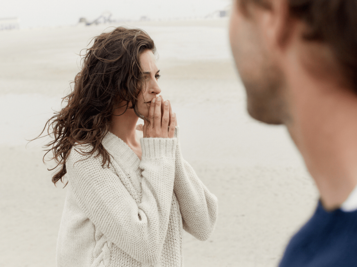 Frau steht am Strand und schaut nachdenklich in Ferne.