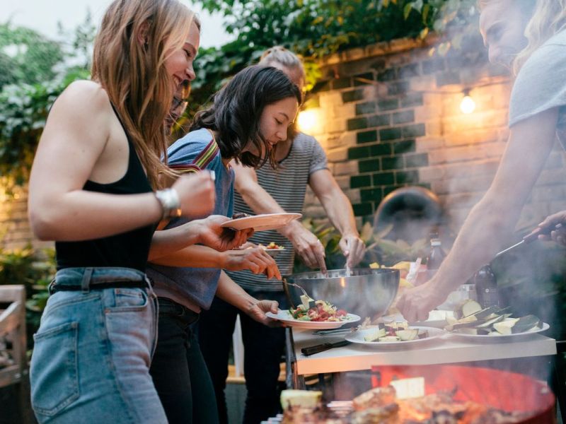 Freunde stehen um einen Grill herum und machen eine Grillparty