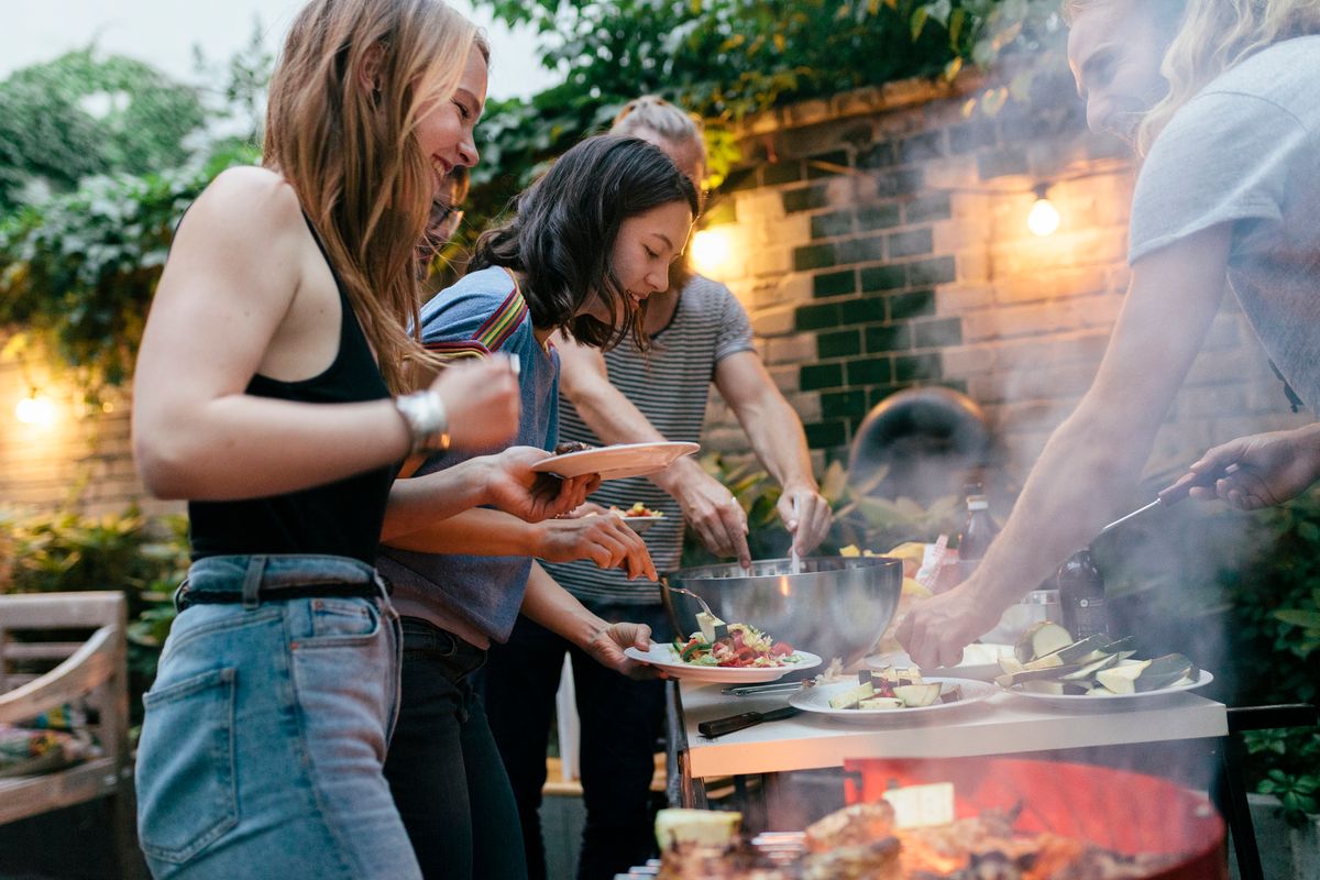 Freunde stehen um einen Grill herum und machen eine Grillparty