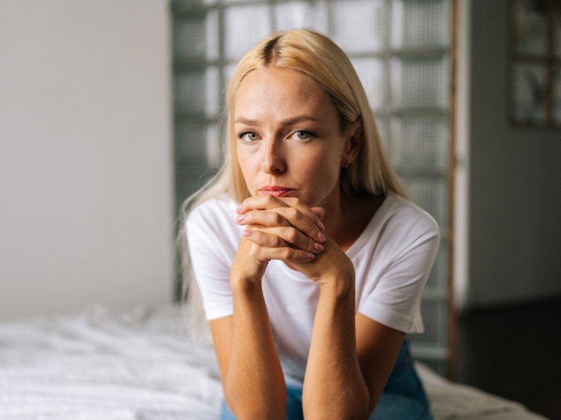 Blonde Frau auf einem Bett, die ernst und nachdenklich in die Kamera schaut