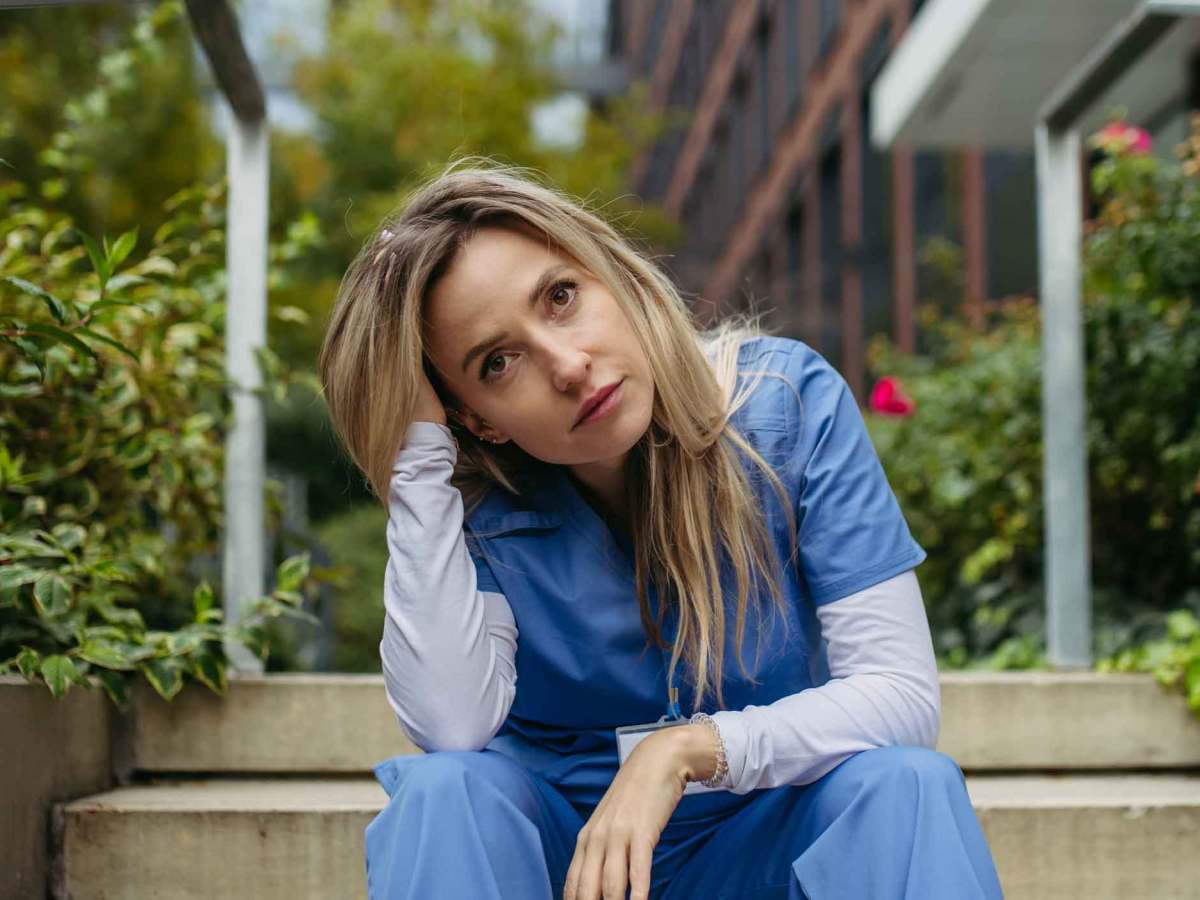 Junge Frau mit OP-Kasack sitzt drau&szlig;en und ist verzweifelt.