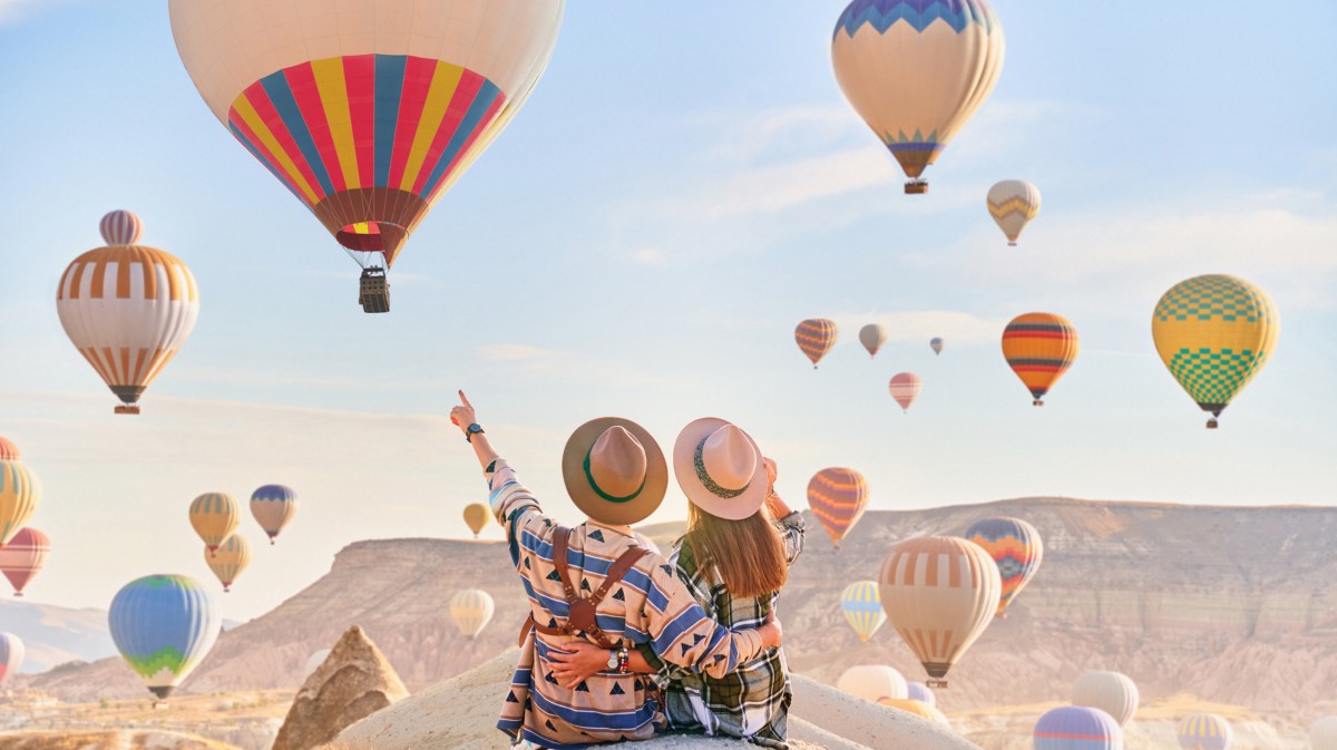 Frau und Mann auf einem Felsvorsprung umgeben von Heißluftballons