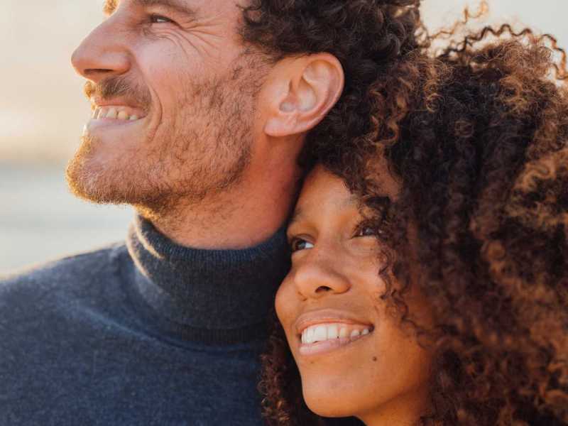 Junge Frau schmiegt sich an ihren Partner. Beide lächeln.