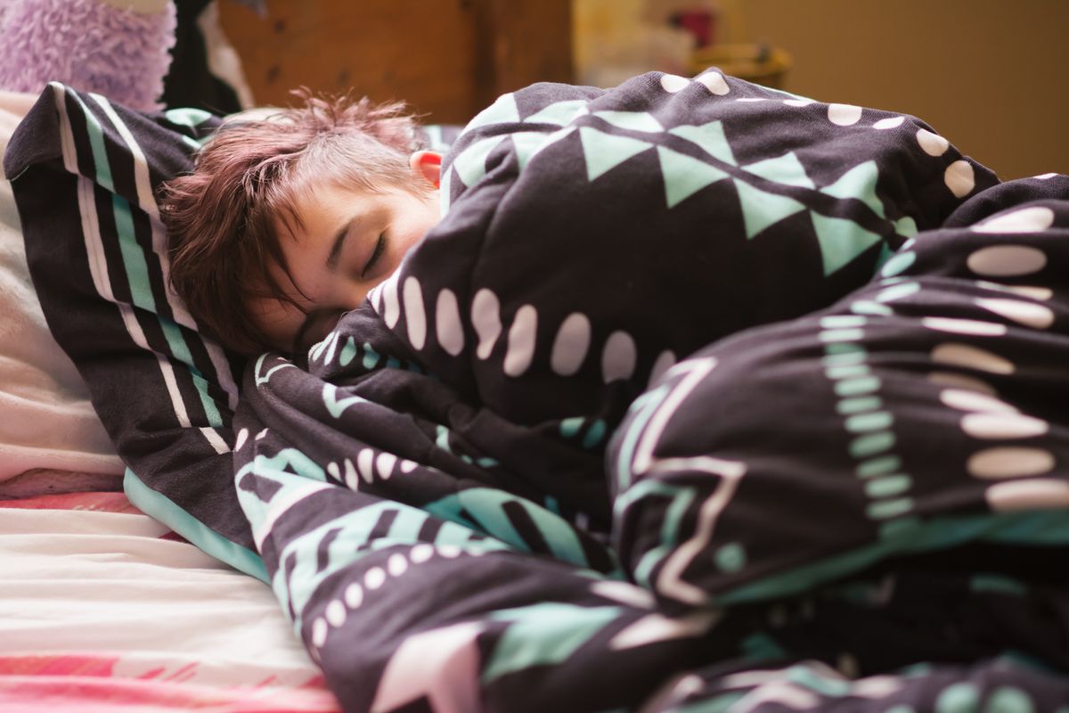 Teenager liegt tagsüber eingekuschelt in seinem Bett und schläft.