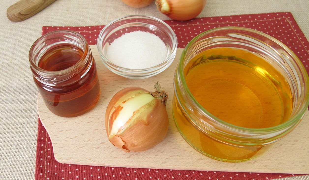 Selbst gemachter Zwiebelsaft und eine Zwiebel als Reizhusten-Hausmittel auf einem Holzbrett.