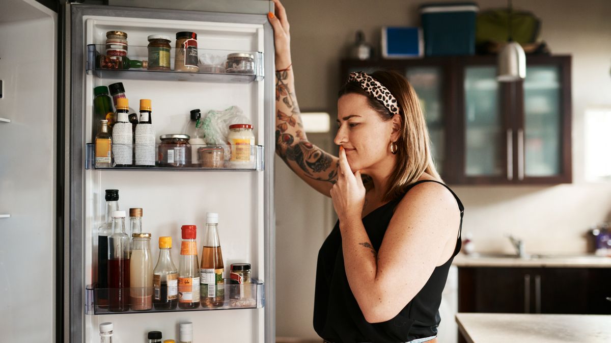 Frau steht am Kühlschrank und überlegt, was sie essen möchte