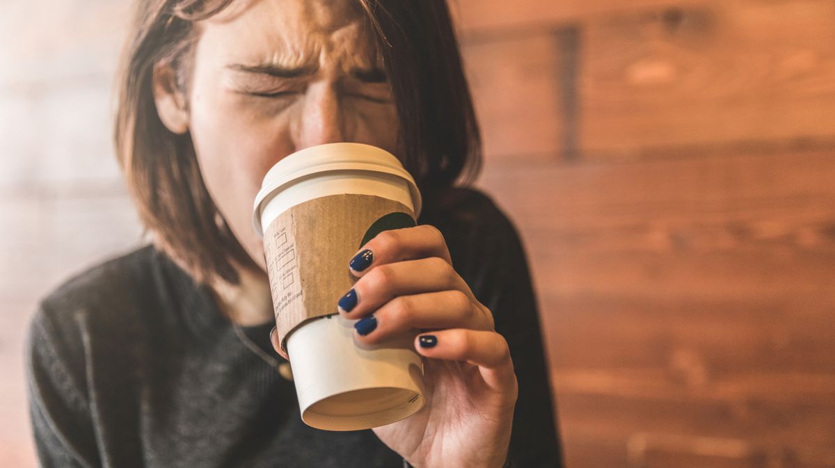 Junge Frau trinkt einen Kaffee und verbrennt sich die Zunge