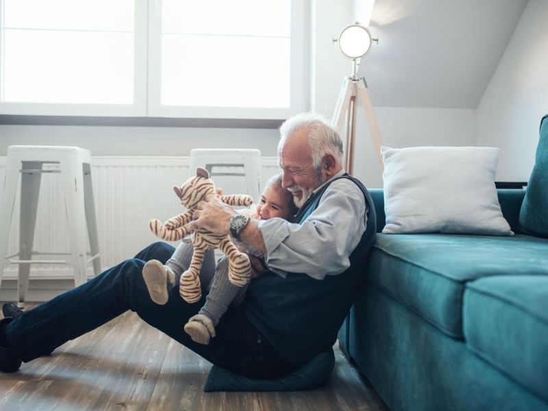 Großvater und Enkeltochter spielen im Wohnzimmer zusammen.