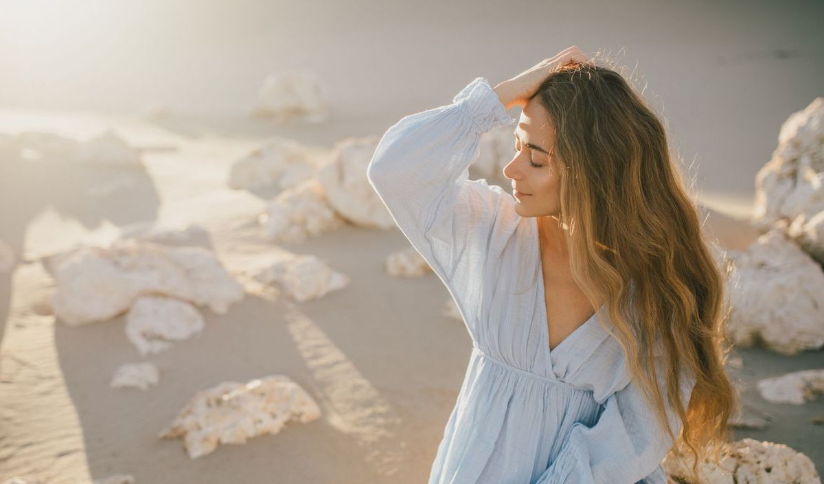 Frau bei Sonnenschein am Strand, die sich lässig durch die Haare geht 