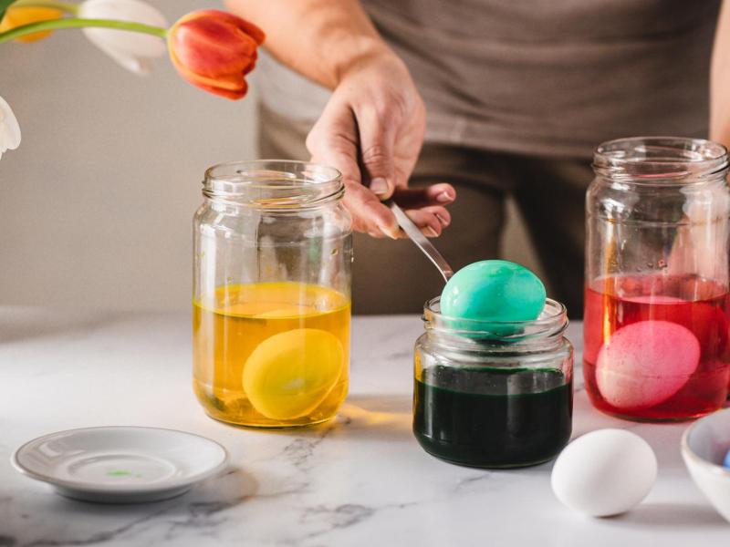 Frau färbt Eier in Gläsern.