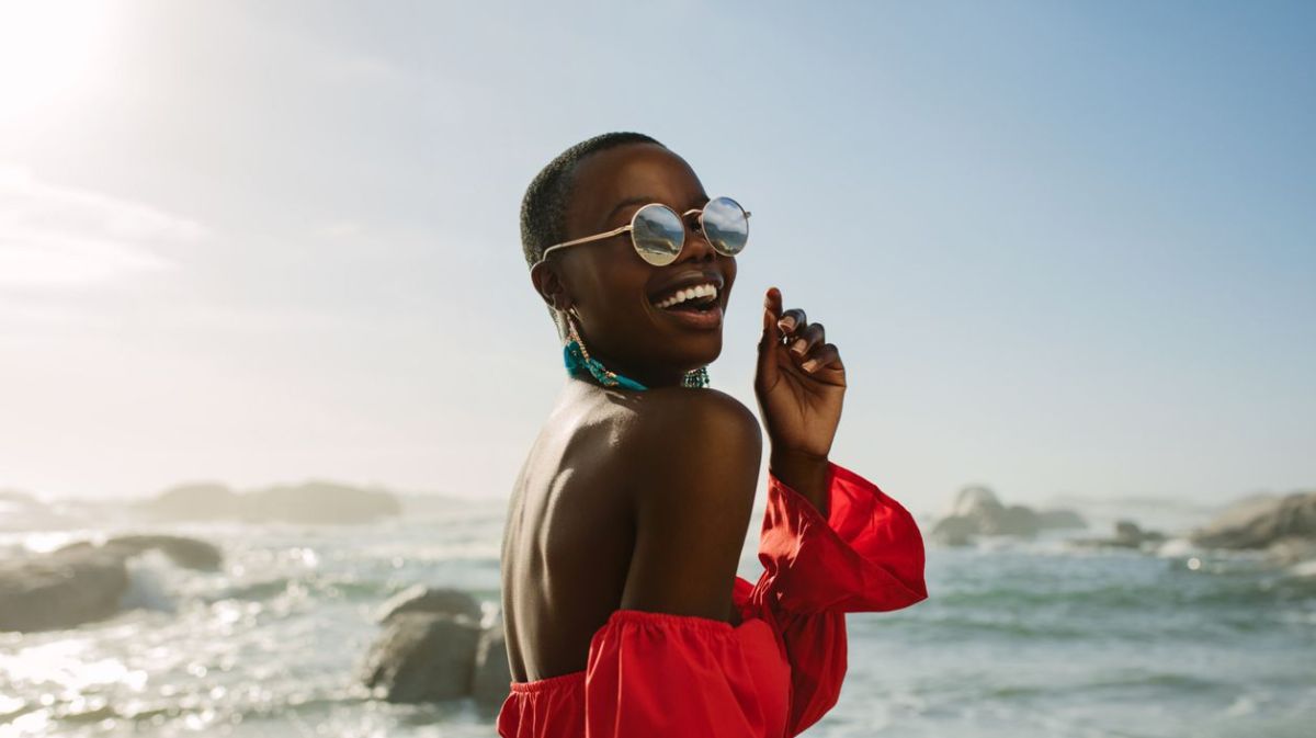 Frau am Strand mit Sonnenbrille am lachen