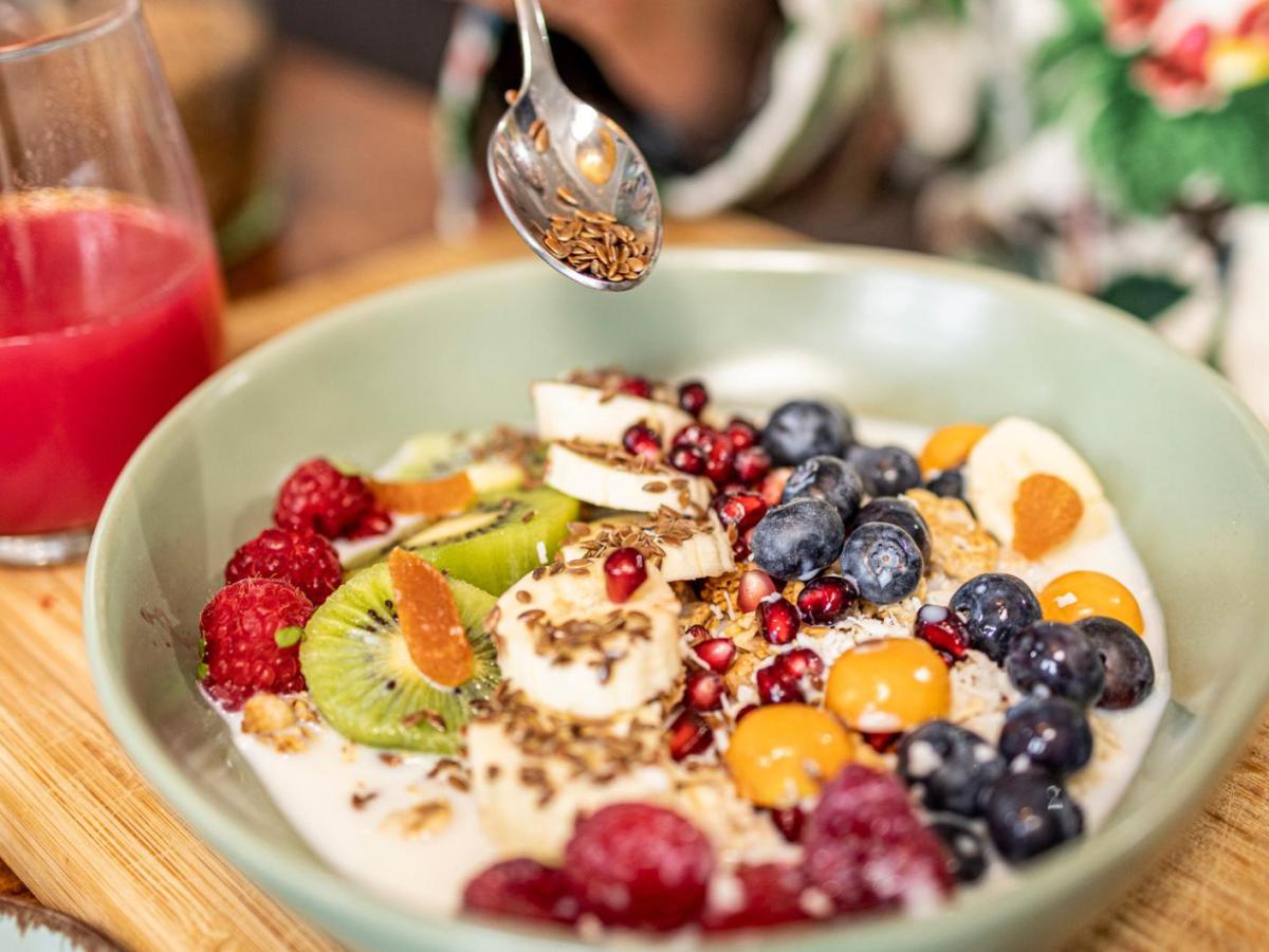 Frau gibt einen Teel&ouml;ffel Leinsamen in die Obstbowl zum Fr&uuml;hst&uuml;ck.