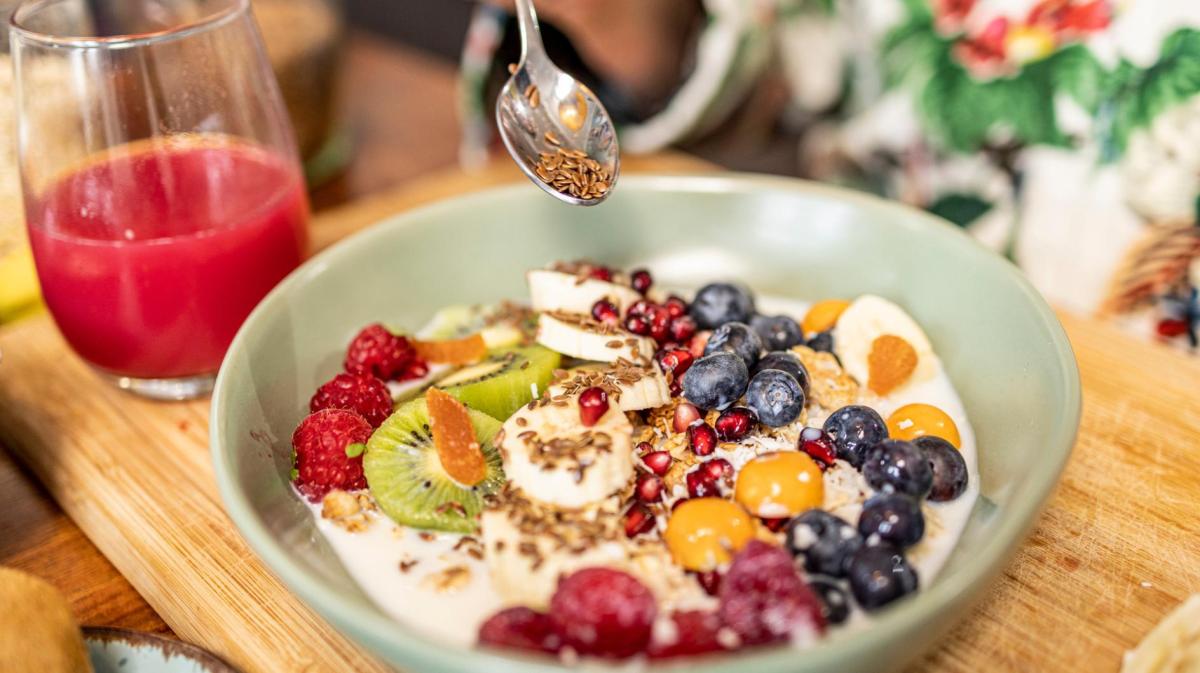 Frau gibt einen Teelöffel Leinsamen in die Obstbowl zum Frühstück.