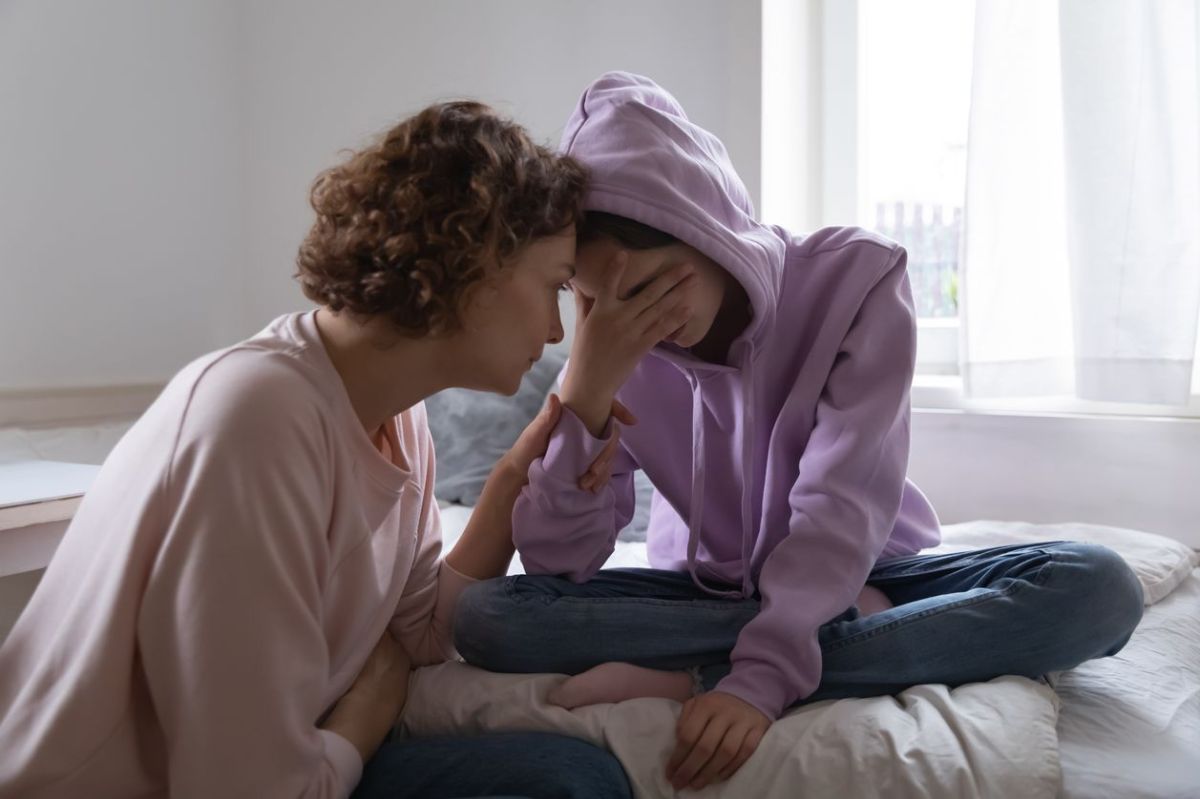 Mutter tröstet ihre Tochter, die weinend auf dem Bett sitzt.