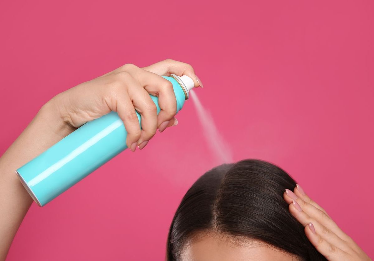 Frau spr&uuml;ht sich die Haare mit Trockenshampoo ein.