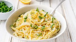 Weißer Teller mit Spaghetti, Zitronenabrieb und Parmesan.