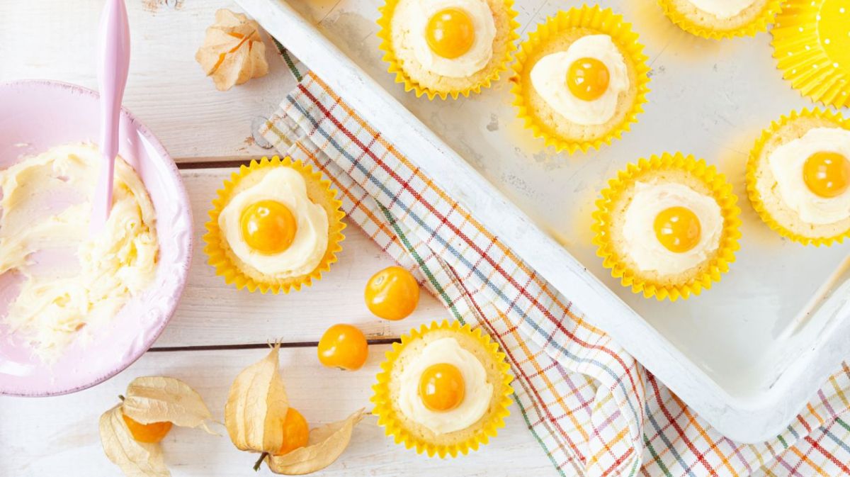 Cupcakes mit Creme und Physalis-Hälfte obendrauf auf Backblech.