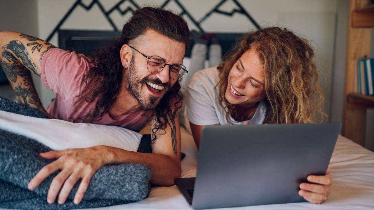 Pärchen auf dem Bett, lachend, mit Laptop