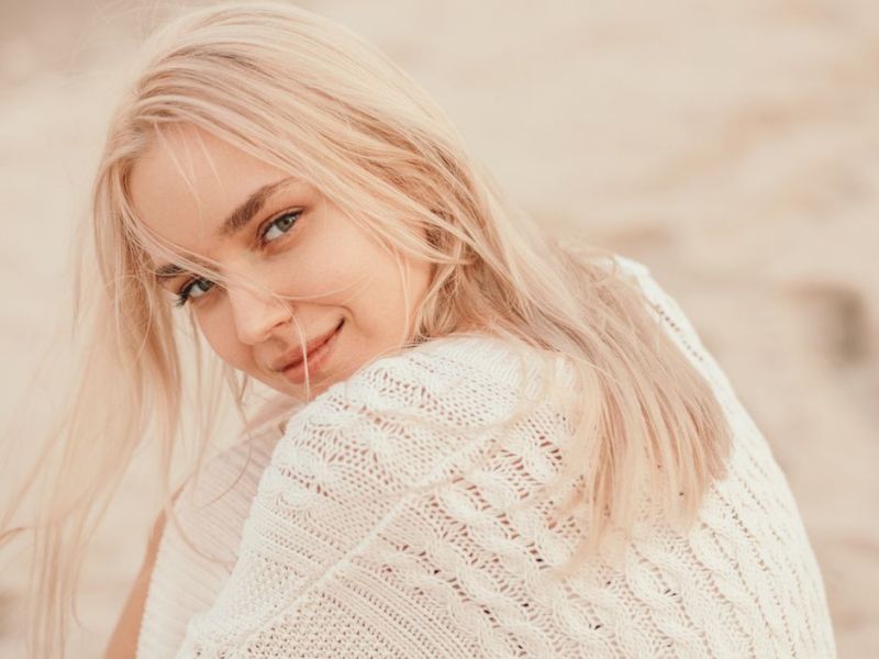 Frau mit blonden Haaren sitzt am Strand und schaut in die Kamera.