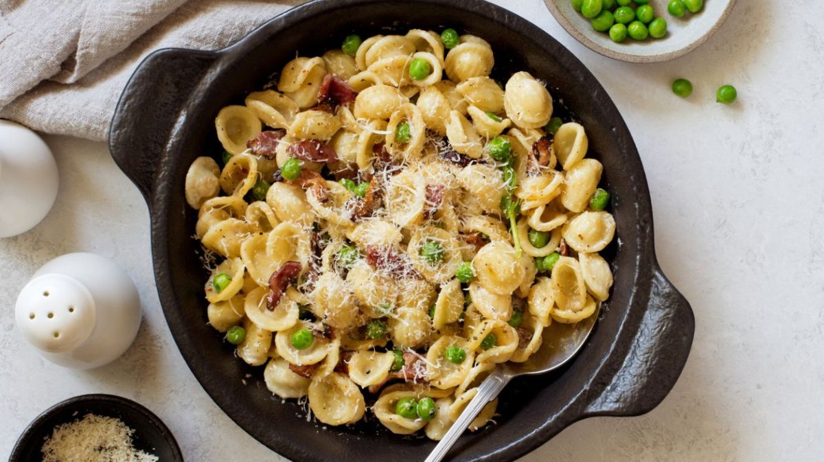 Nudeln mit Erbsen, Speck und Parmesan in einer schwarzen Gusseisenpfanne.