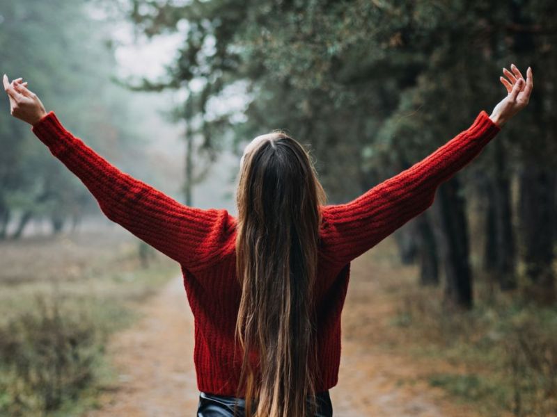 Frau mit langen braunen Haaren steht im Wald.