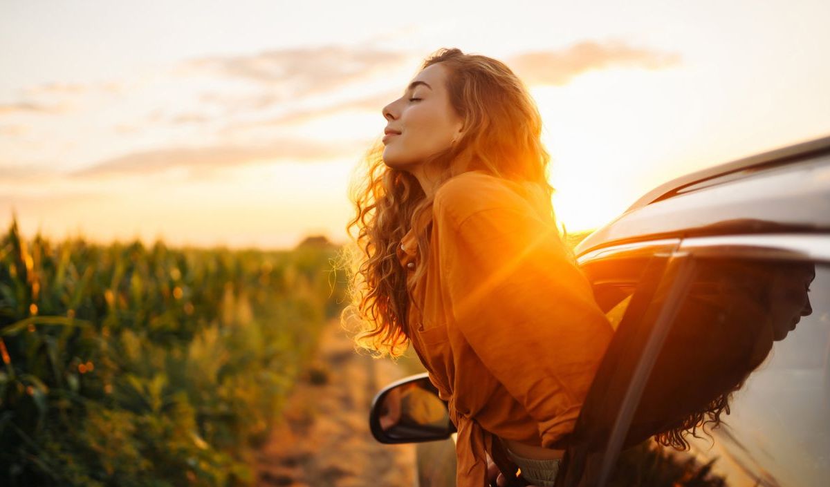 Frau, die sich aus dem Fenster im Auto lehnt und die Sonnenstrahlen genießt