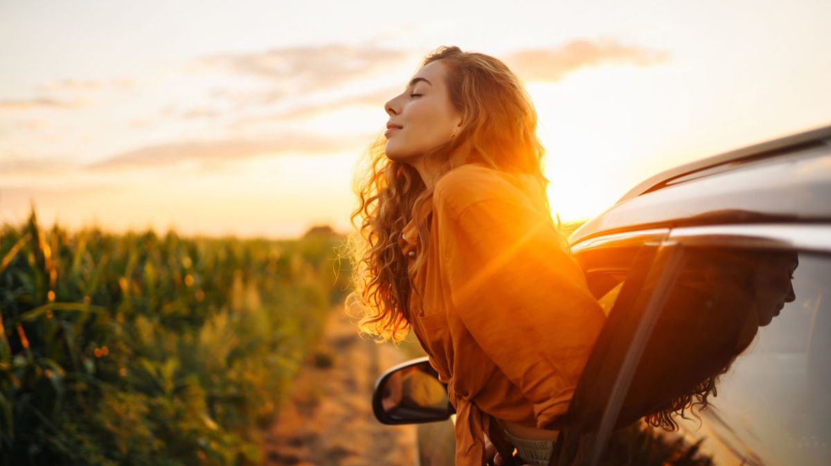 Frau, die sich aus dem Fenster im Auto lehnt und die Sonnenstrahlen genießt