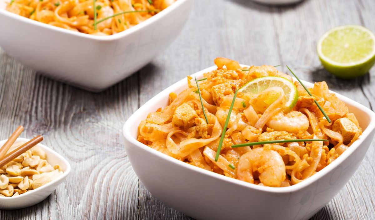 Pad Thai mit Shrimps und Limetten in weißen Schüsseln.