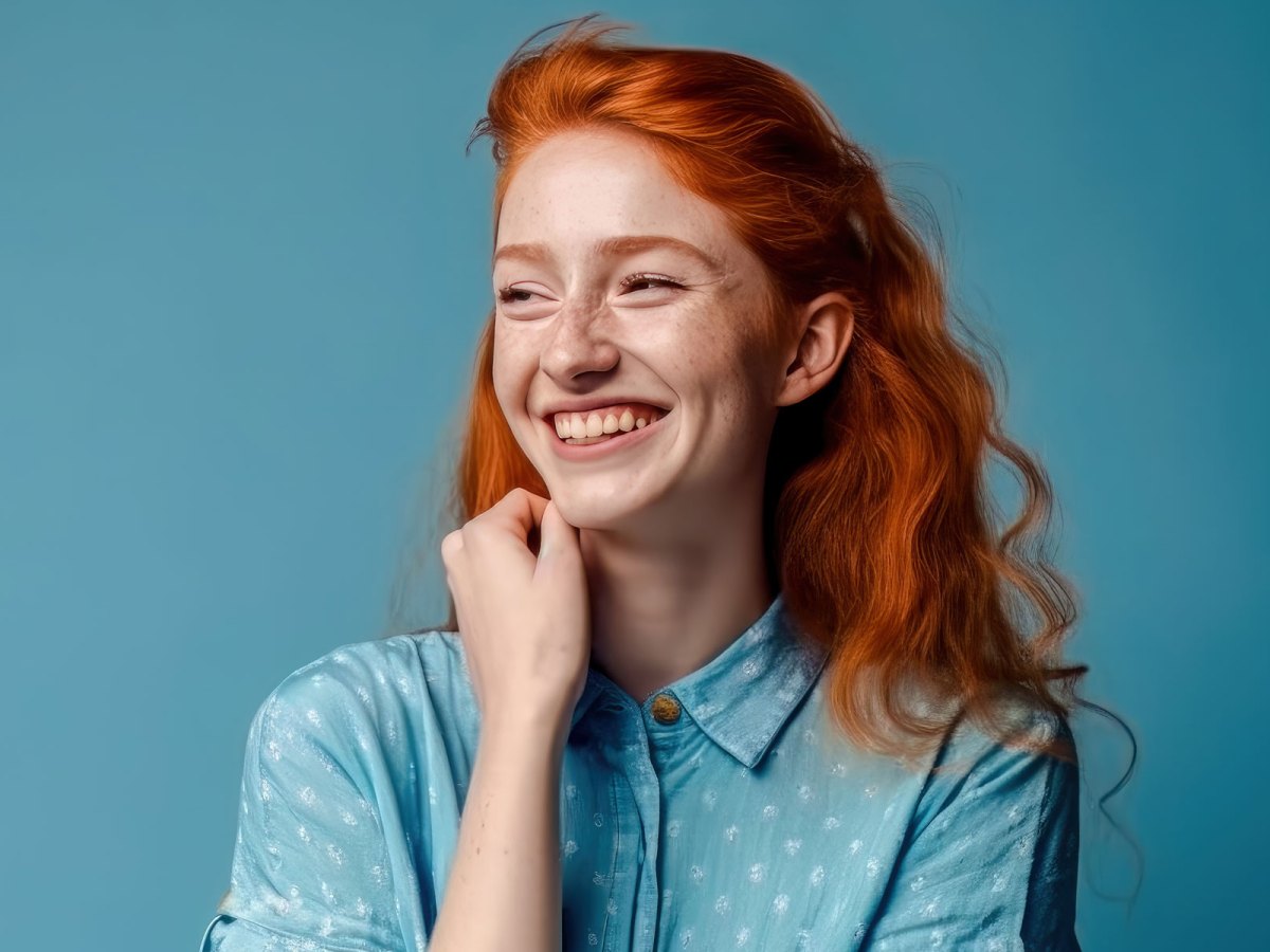 Junge Frau mit roten Haaren schaut lächelnd zur Seite.
