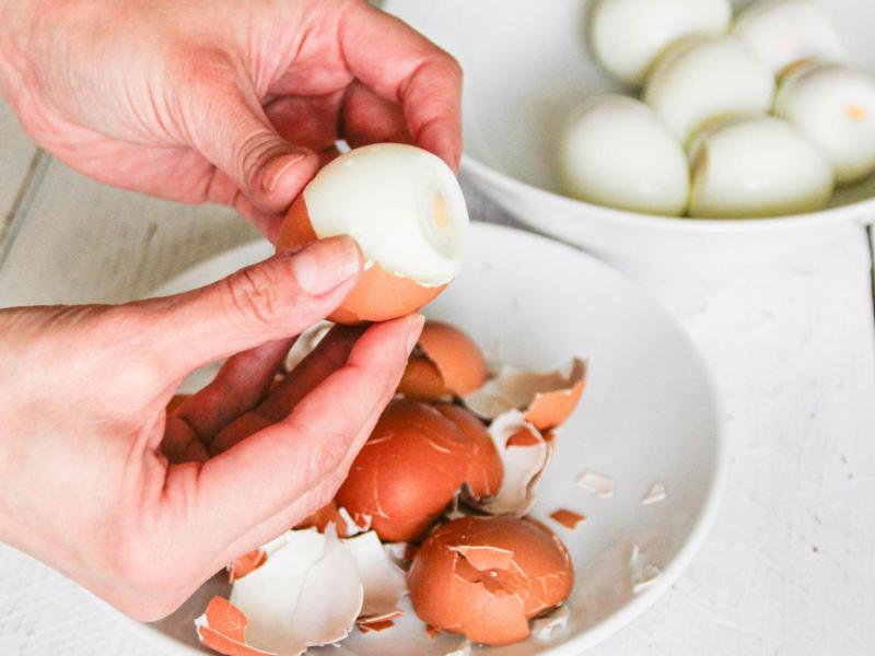 Frau pellt hartgekochte Eier. Daneben steht eine Schüssel voller gepellter Eier.