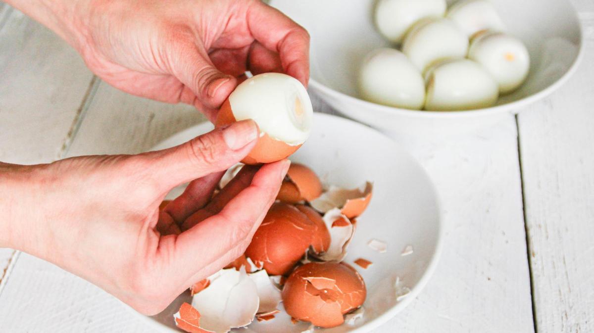 Frau pellt hartgekochte Eier. Daneben steht eine Schüssel voller gepellter Eier.