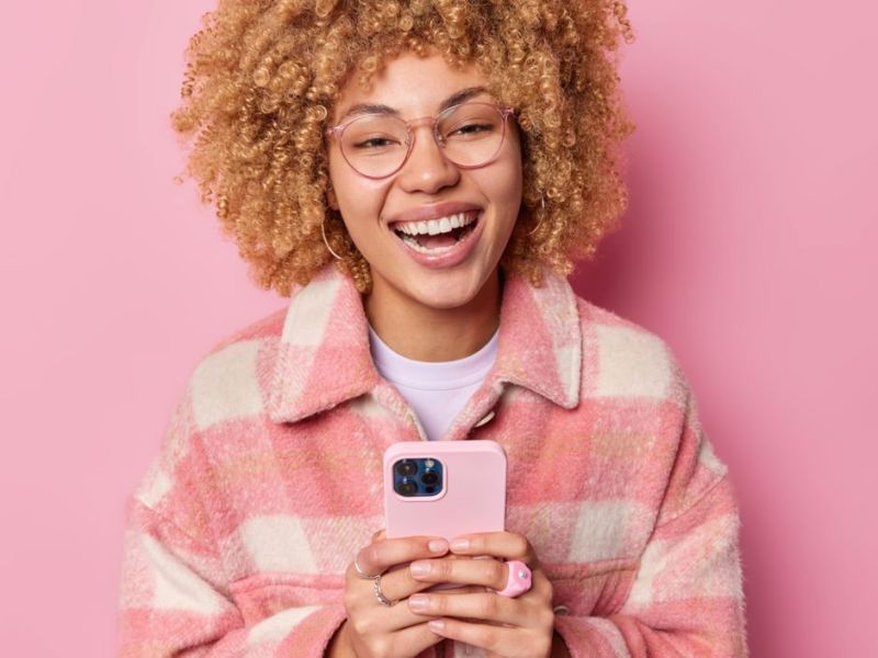 Junge Frau mit pinker Jacke hält Smartphone in der Hand.