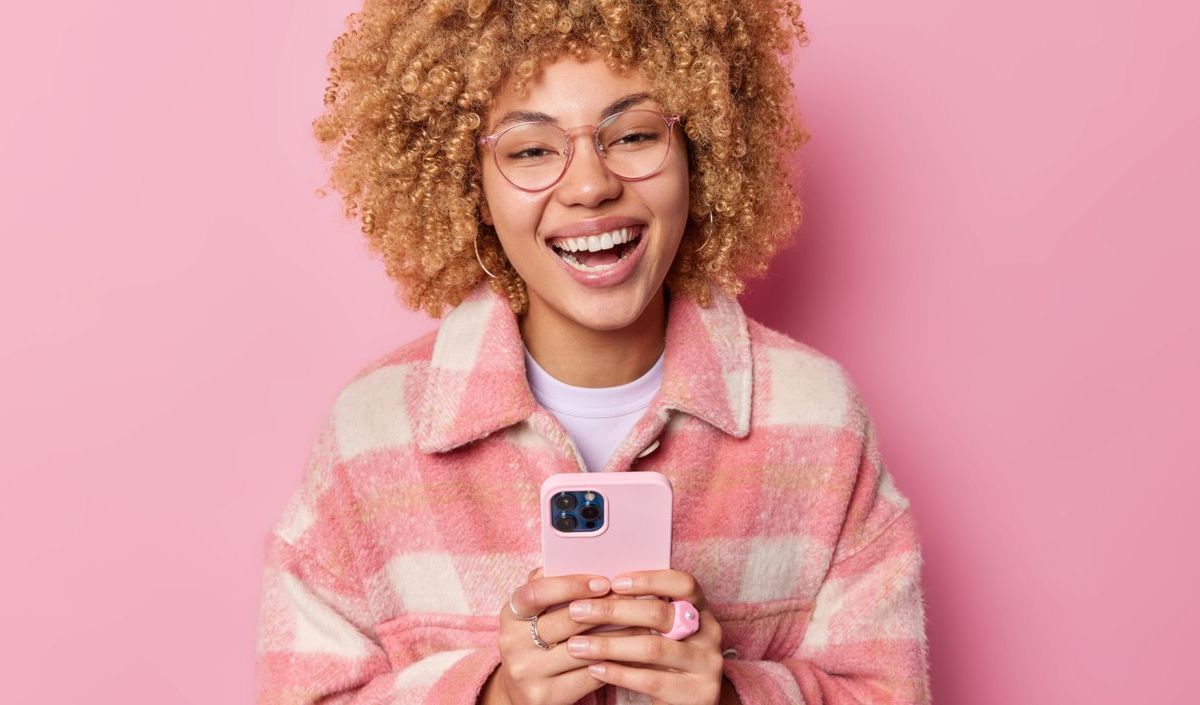 Junge Frau mit pinker Jacke hält Smartphone in der Hand.