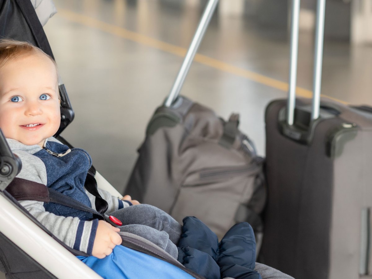 Kleines Baby sitzt im Kinderwagen, neben ihm stehen zwei Koffer.