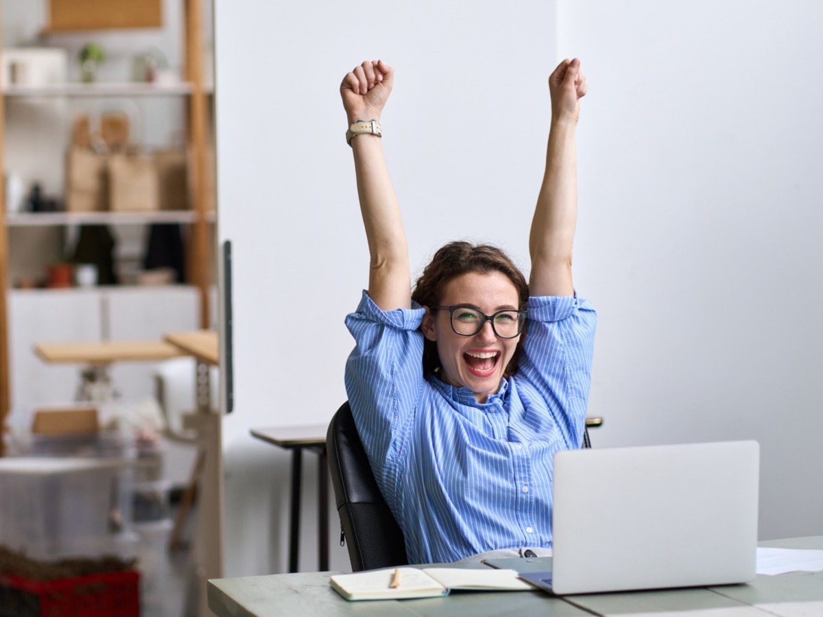 Frau auf der Arbeit, reißt die Arme in die Luft und freut sich.