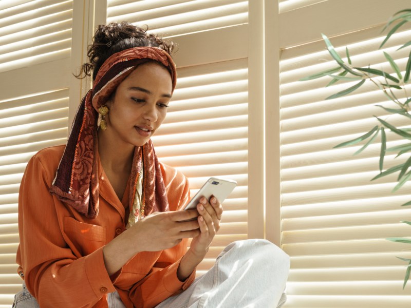 Frau auf Fensterbank mit Handy in der Hand