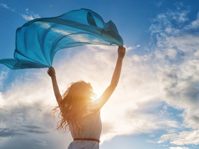 Frau hält Tuch in die Luft, blauer Himmel