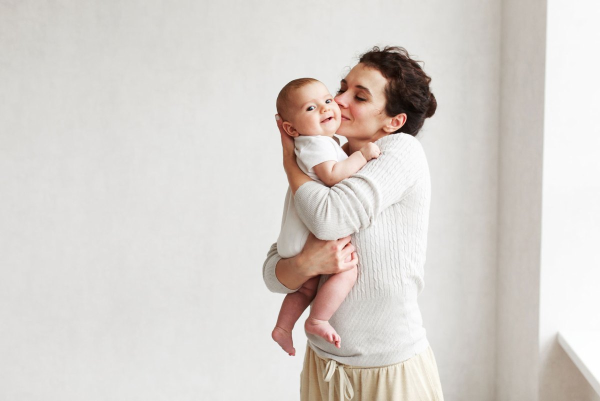 Frau hält Baby auf dem Arm und küsst es.