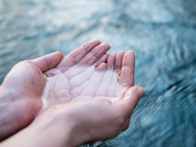 Wasser in zusammengehaltenen Händen über einem fließenden Strom. 