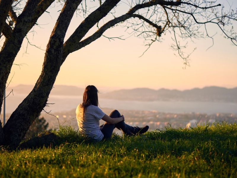 Frau sitzt alleine beim Sonnenuntergang unter einem Baum