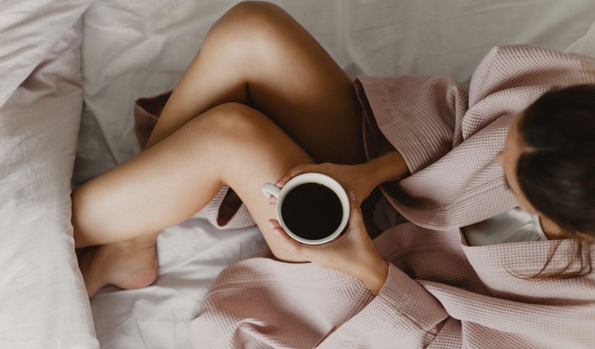 Frau liegt mit Tasse Kaffee im Bett