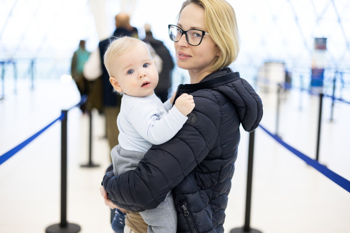 Mutter trägt ihr Baby auf dem Arm und beide stehen in der Schlange der Passkontrolle am Flughafen.