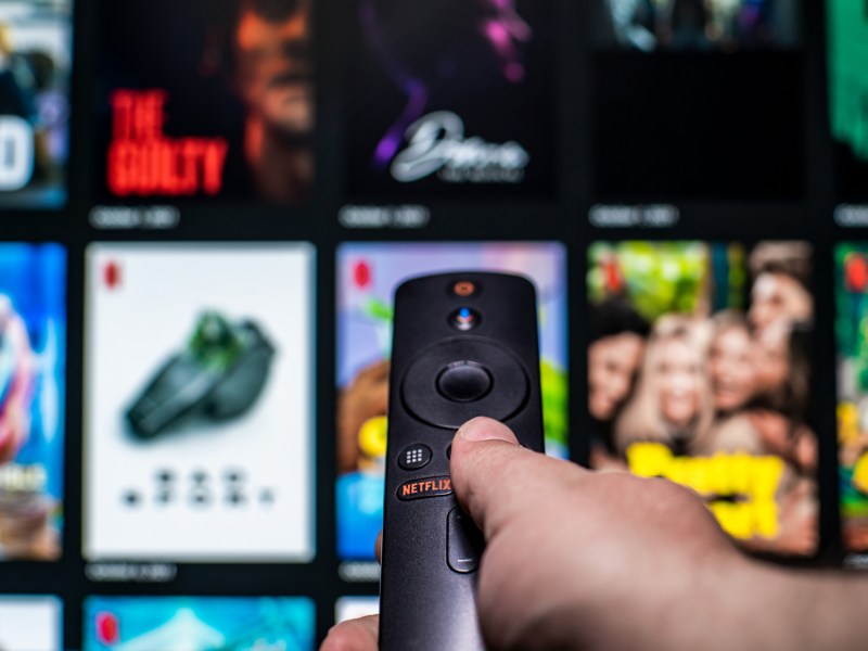 Mann mit Fernbedienung in der Hand und einem Netflix Bildschirm im Hintergrund