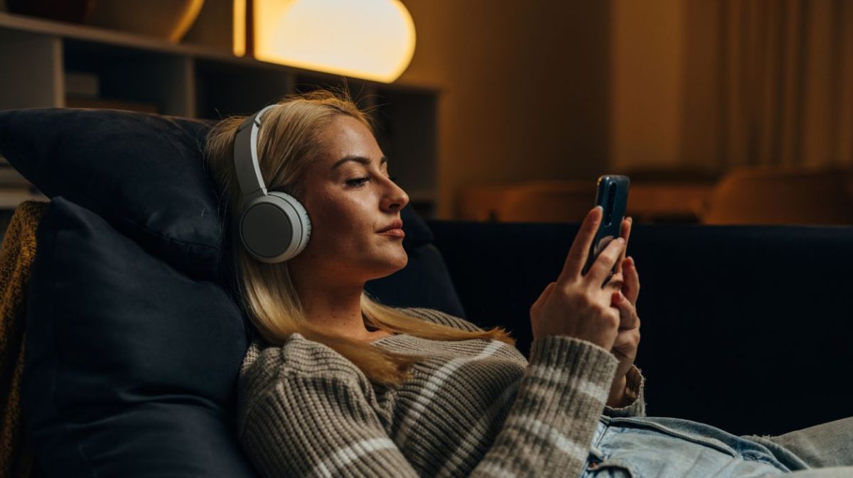 Frau sitzt gemütlich auf der Couch mit Handy in der Hand