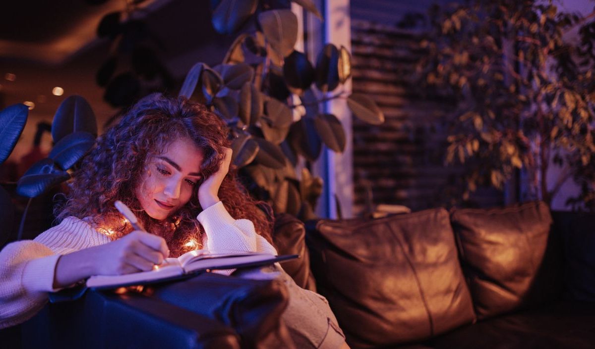 Frau sitzt in der Nacht auf dem Sofa und schreibt in ein Buch 
