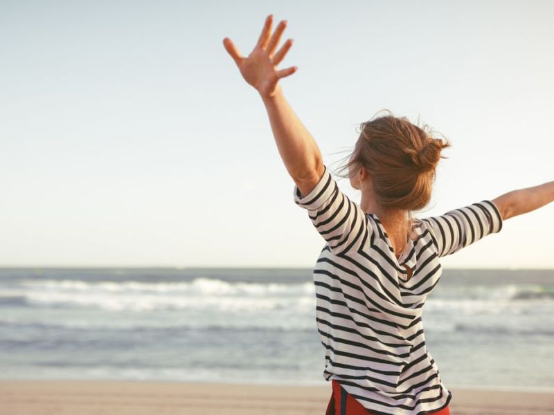 Frau mit ausgebreiteten Armen am Strand 