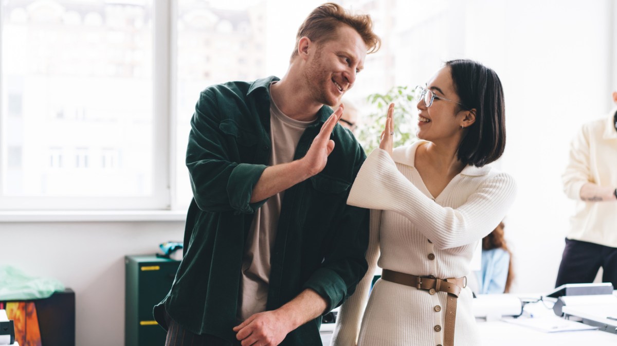 Junger Mann und Frau geben sich auf Arbeit ein High Five.