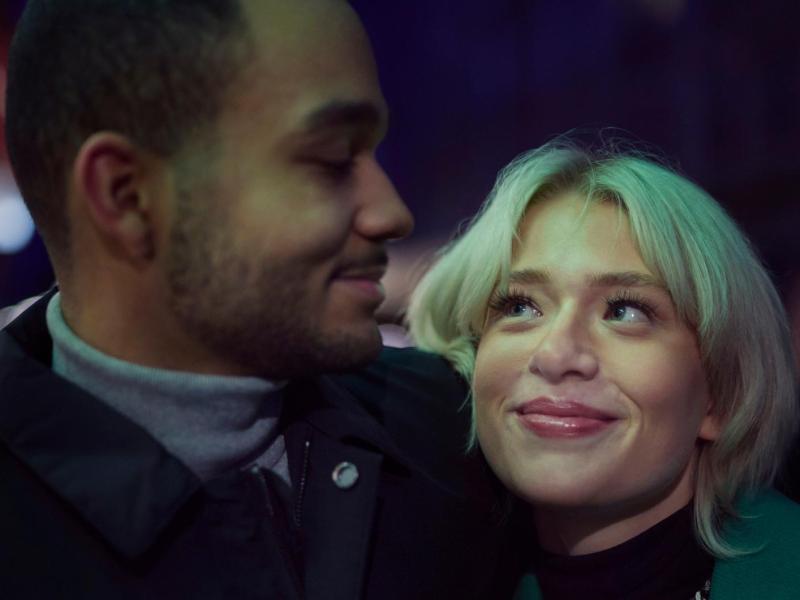 Ein junges Paar blickt sich lächelnd an, die Frau mit blondem Haar schaut verliebt hoch, während der Mann sanft zurücklächelt.